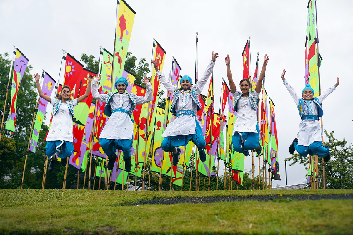 Hardeep and bhangra dancers jumping in front of colourful flags