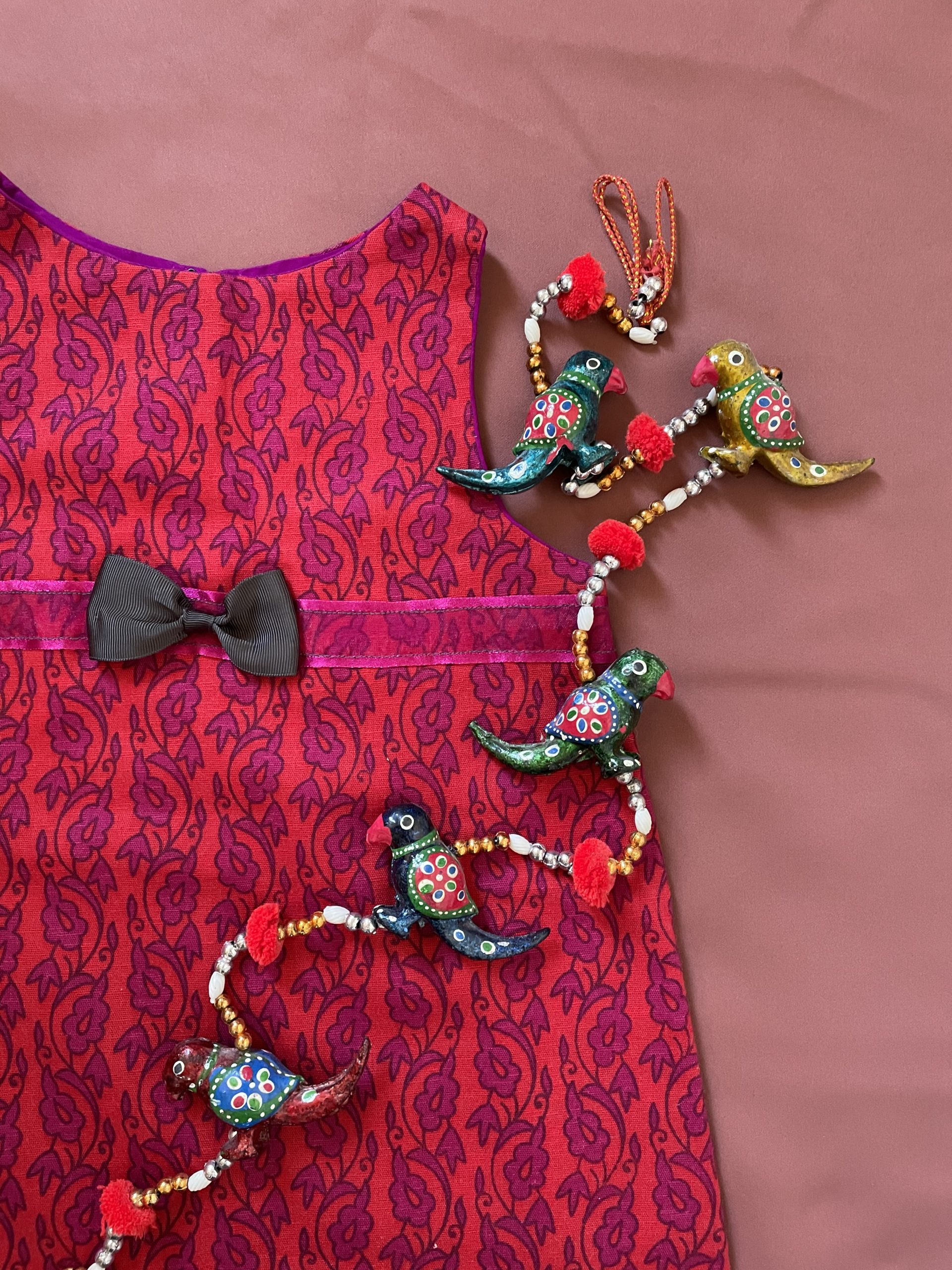 Child's dress on a tables, photographed from above with a beaded hanging including pained bird shapes lying across it