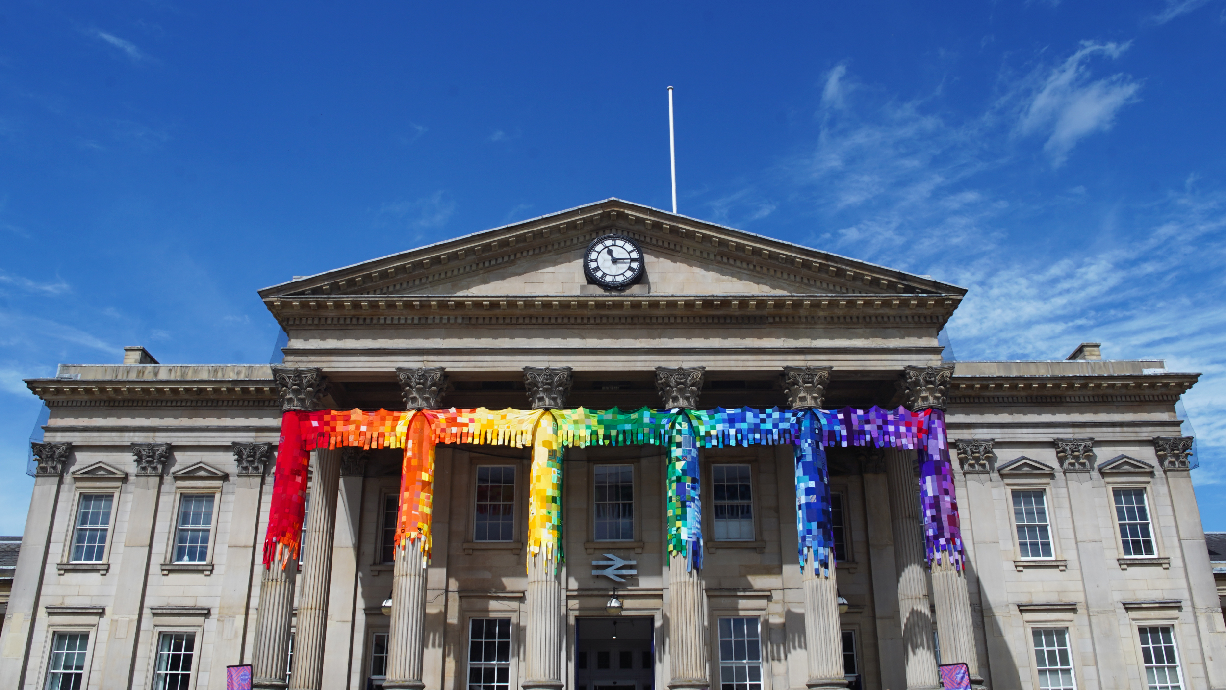 Front of Huddersfield Train Station showing the knitted rainbow decoration on the pillars