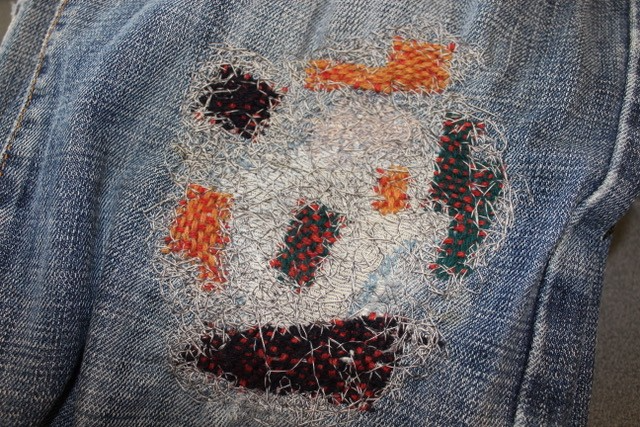 A close up of denim fabric that has been repaired using darning and stiches