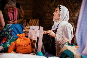 A person wearing a headscarf sitting a table stitching. The table has a display of different fabrics and a sign saying 6million +