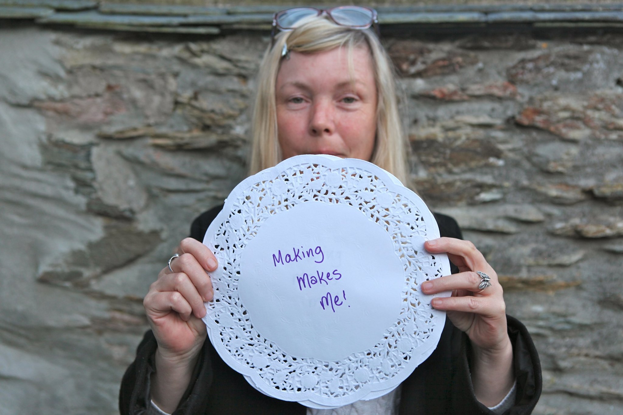 A person holding up a doily which has text written on it that says making makes me