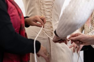 A close up of the back of a corseted dress being tied by hands