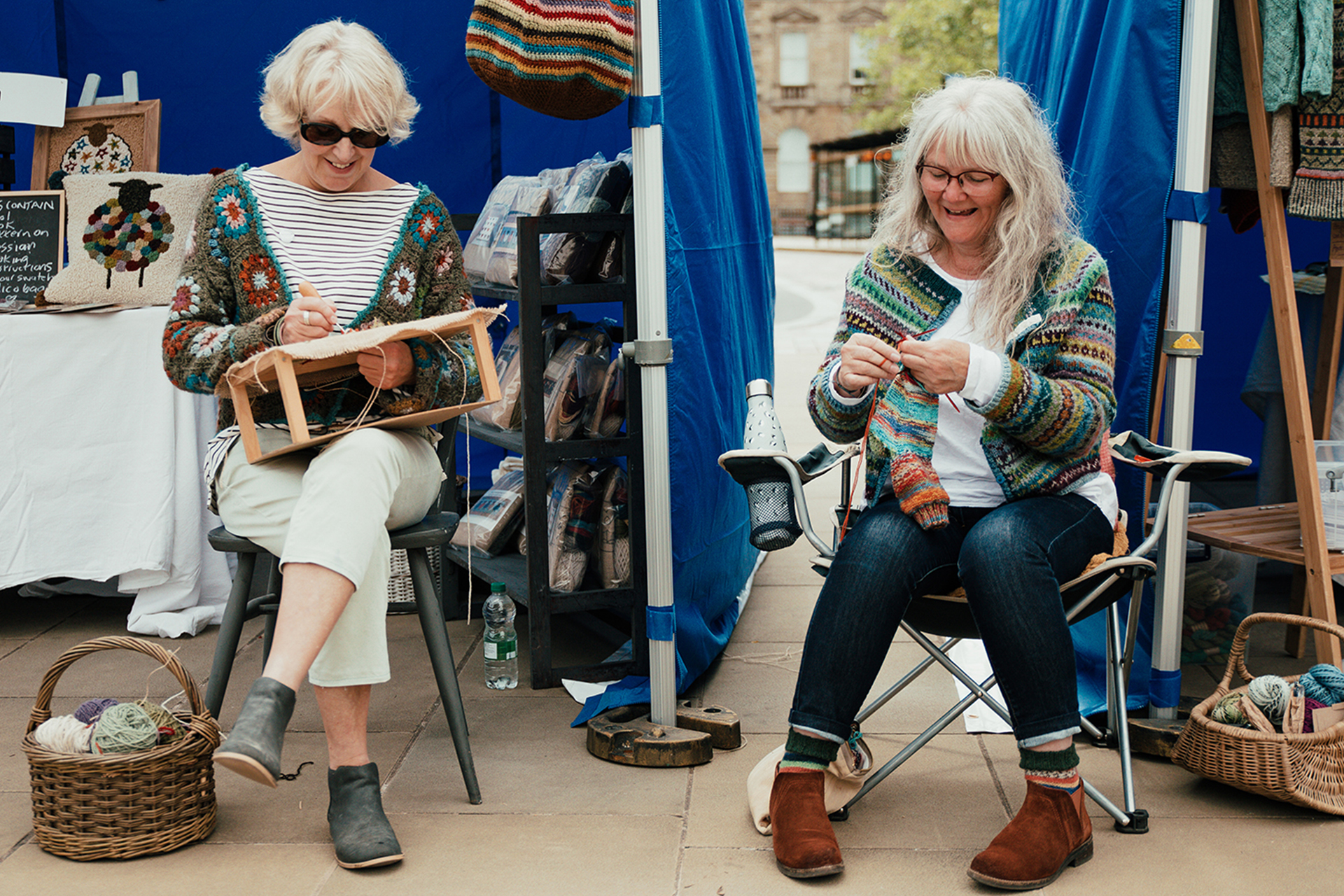 Two people sitting side by side in an outdoor seeting knitting