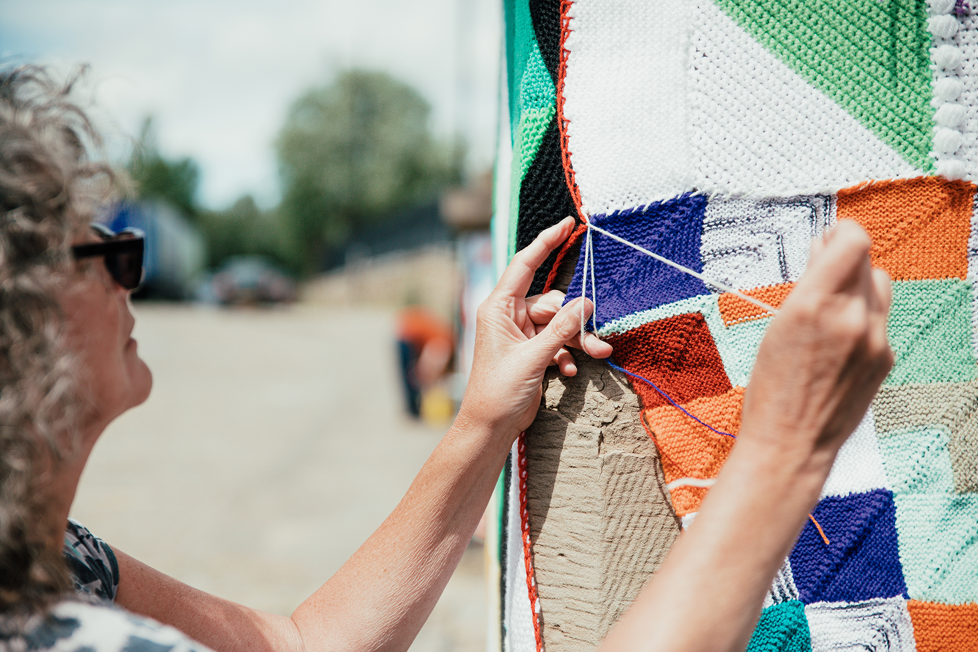 A person tying colourful knitted squares to a post