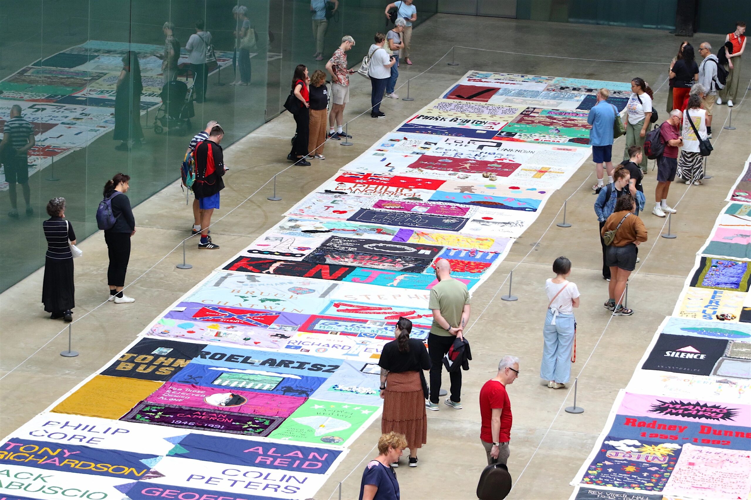 A large display of quilts in a gallery setting with people viewing them