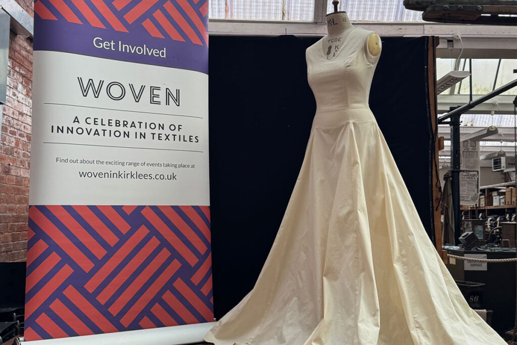 A calico dress on a mannequin next to a large WOVEN banner in a museum setting
