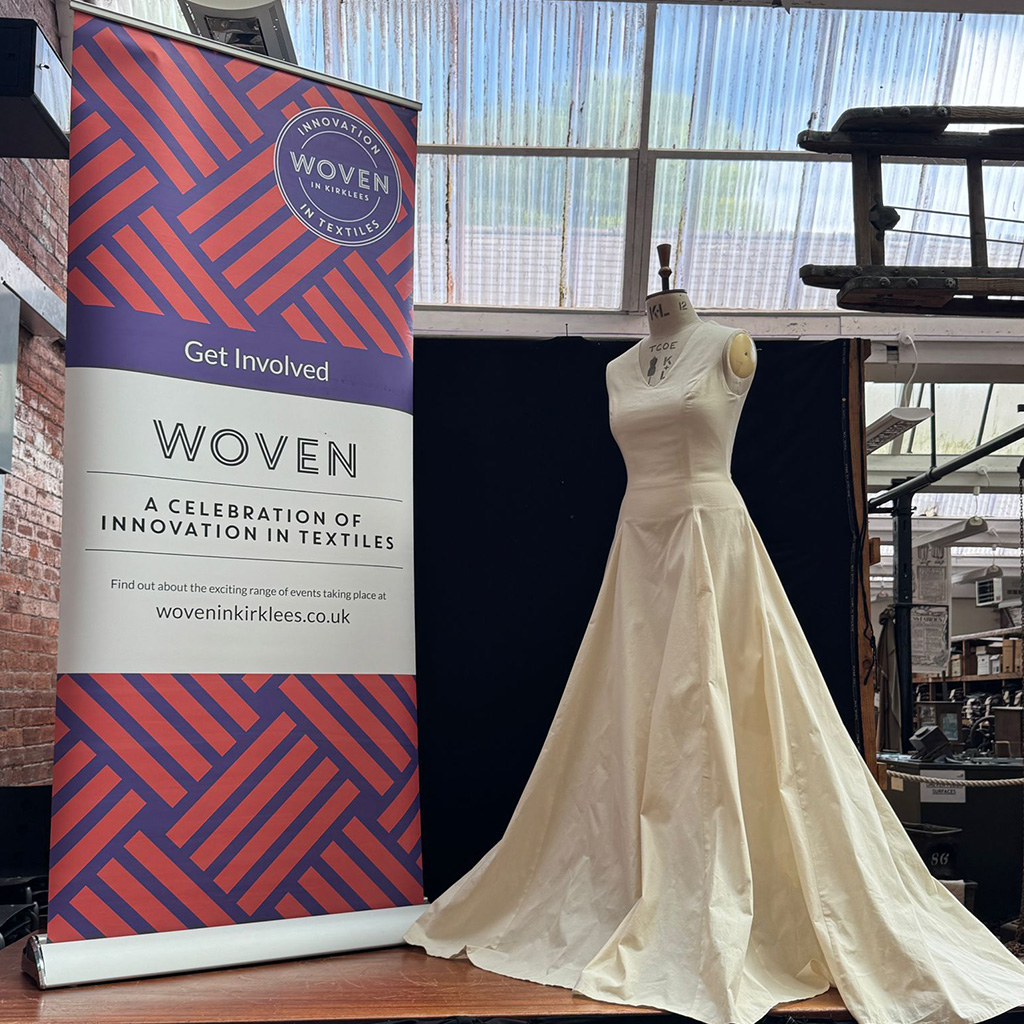 A calico dress on a mannequin next to a large WOVEN banner in a museum setting