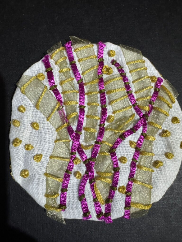 A handmade embroidered textile patch in gold and pink