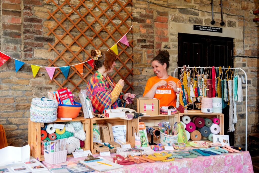 Two people smiling standing at a stall full of colourful textile materials