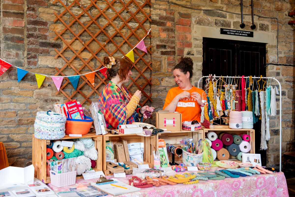 Two people smiling standing at a stall full of colourful textile materials