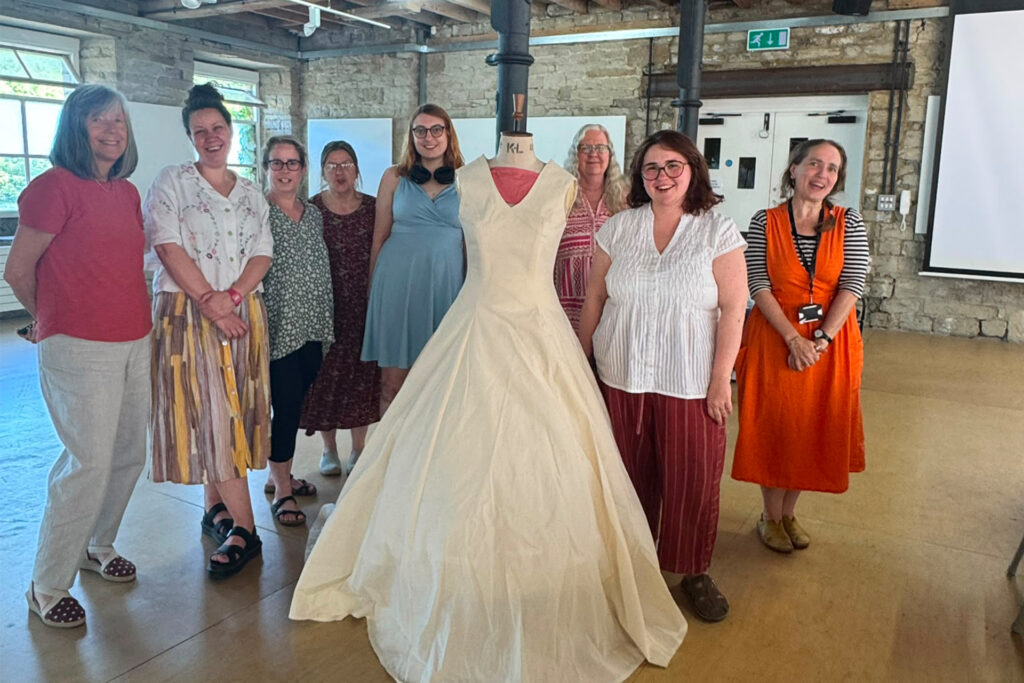 A group of people smiling surrounding a calico dress on a mannequin